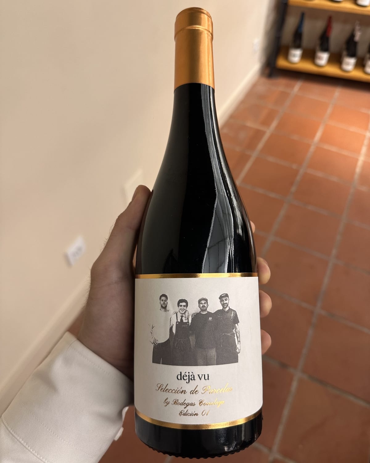 Botella de vino sostenida en una mano, con fotografía de cuatro personas impresa en la etiqueta.